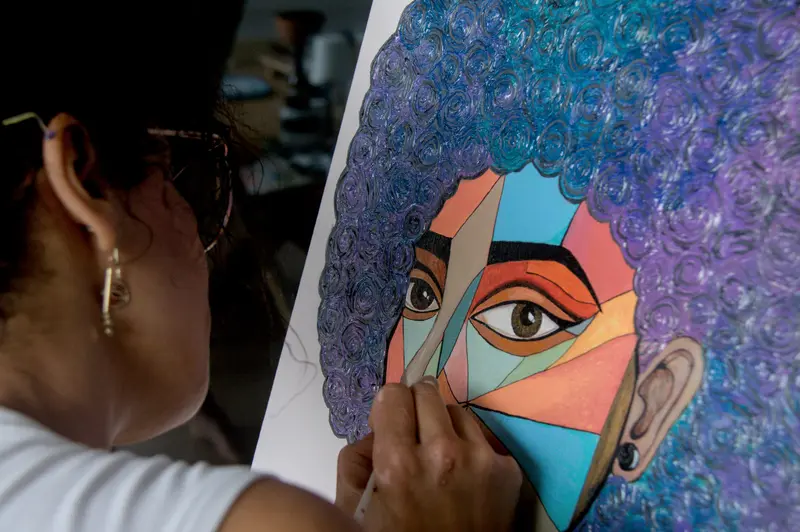 Najlae en su estudio, pintando un retrato de gran formato con cabello de espirales azules y violetas.