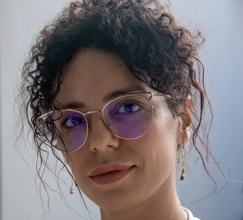 Retrato de Najlae, pintora amazigh: cabello rizado recogido, gafas y media sonrisa.